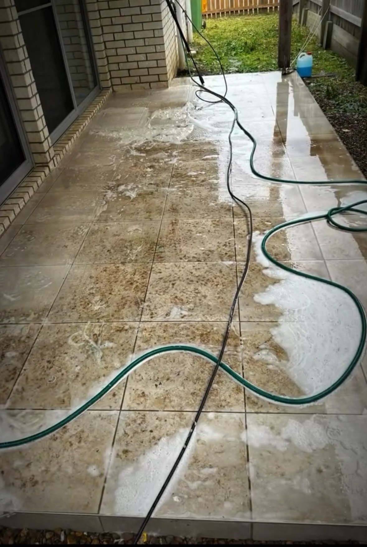 Tiled patio during washing, with hose and cleaning equipment visible